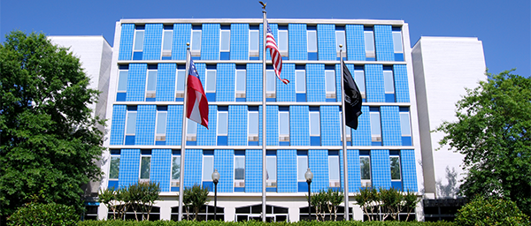 The exterior of the Georgia War Veterans Nursing Home is bright blue, with windows overlooking a plaza with the American, state, and POW flag. 