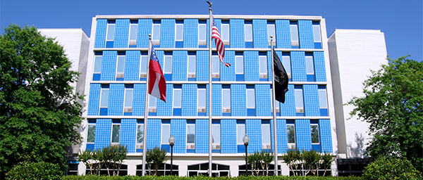 The exterior of the Georgia War Veterans Nursing Home is bright blue, with windows overlooking a plaza with the American, state, and POW flag.