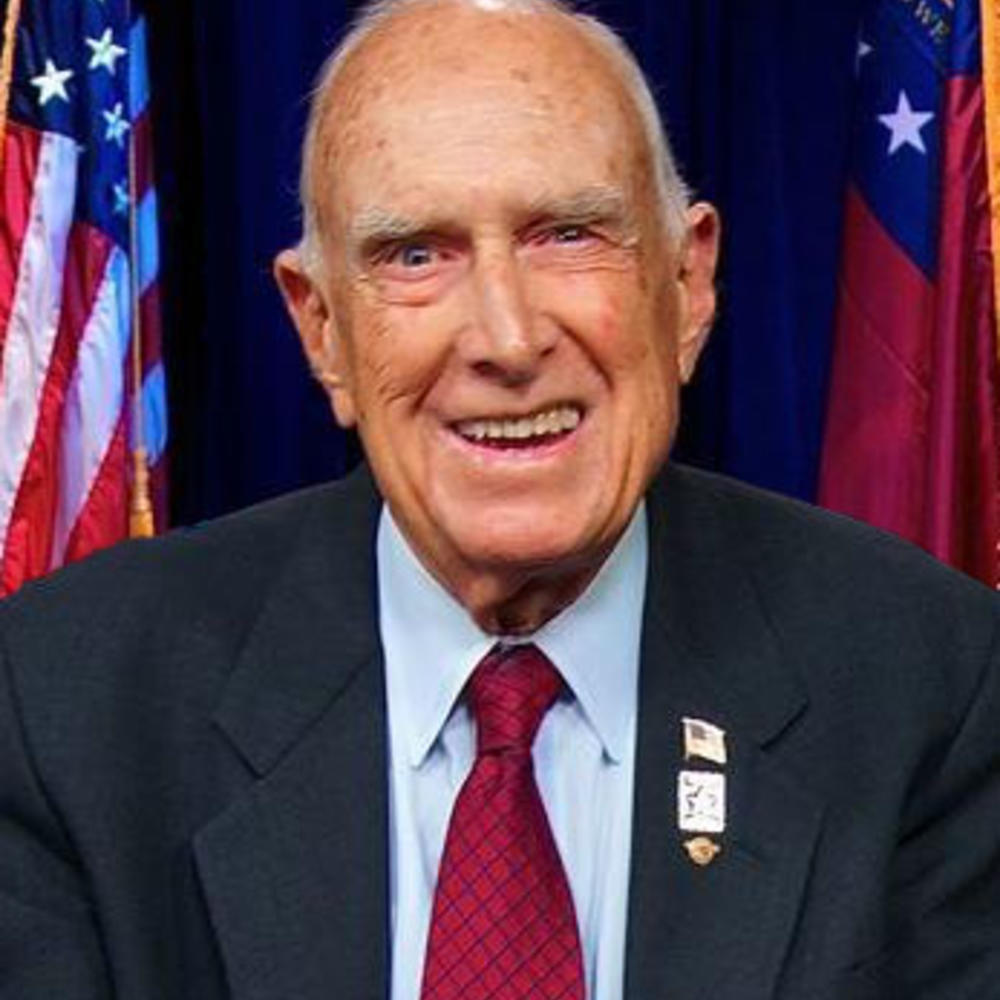 A photo of the late Pete Wheeler in front of an American and state flag.